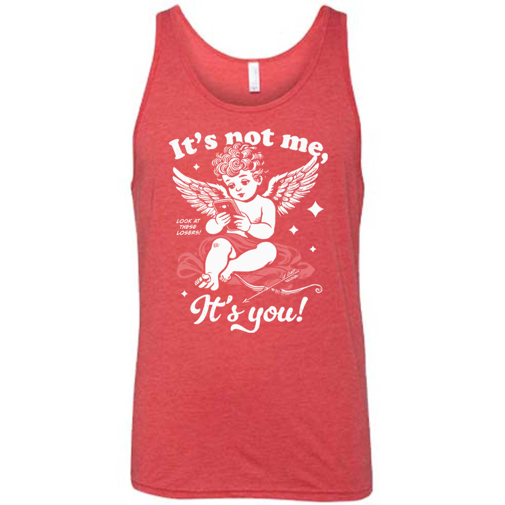 red unisex tank with the words "it's not me, it's you!" on it, with graphics of Cupid looking at a cell phone (presumably looking at dating apps), with small words saying "look at these losers!" and Cupid's bow and arrow at his side