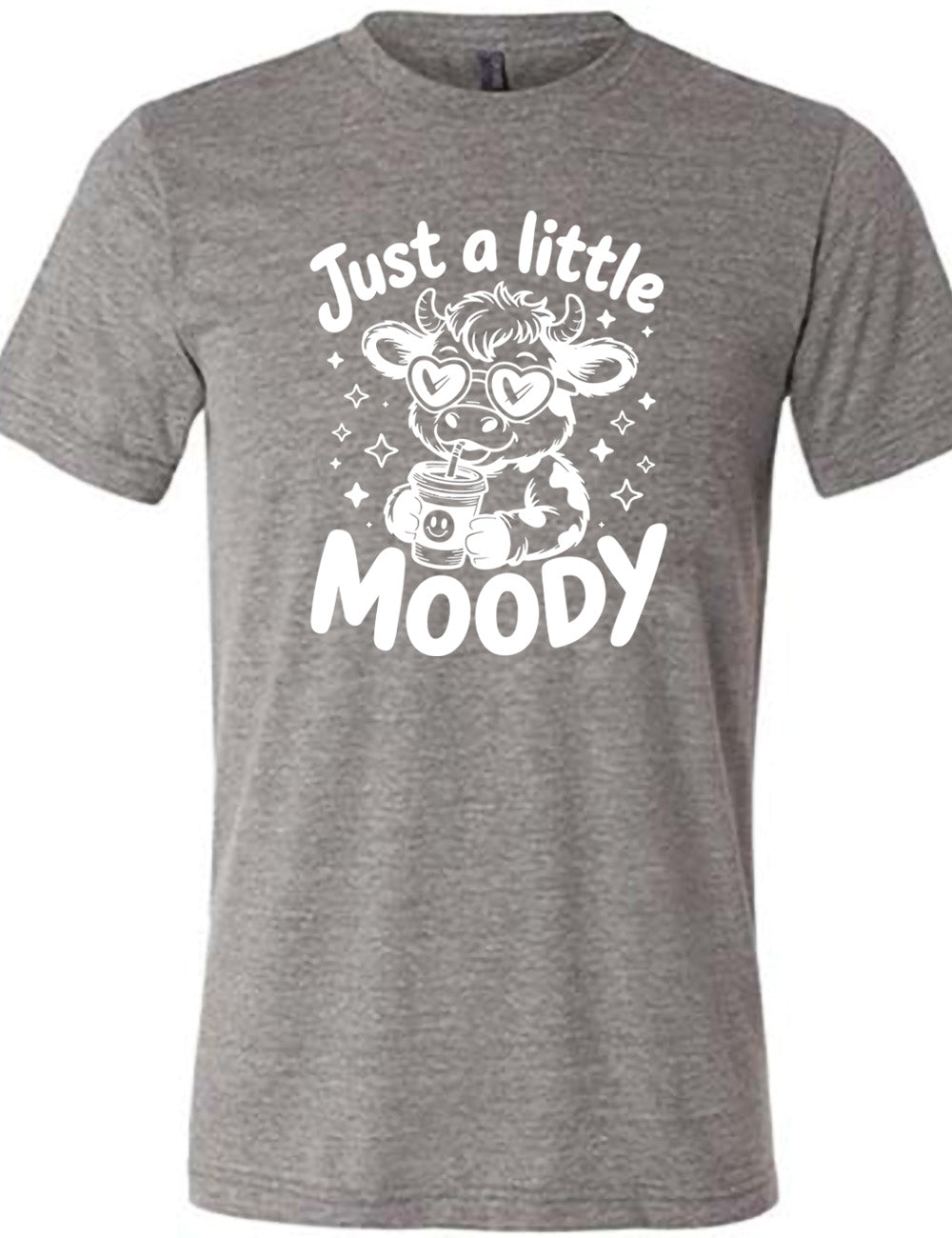 grey unisex tee with the graphic of a cartoon cow, wearing heart sunglasses and drinking out of an iced cup with a straw, surrounded by little stars, as well as the words "just a little moody" around it