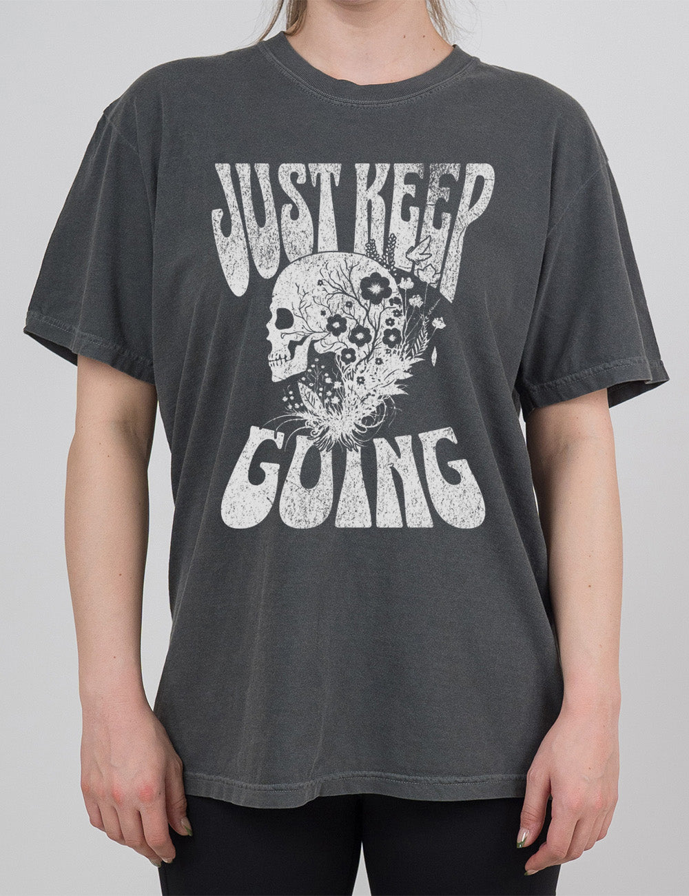 pepper modern tee with print placement on the front, with the words "just keep going" on it, with the graphic of a skull's profile, growing among plants