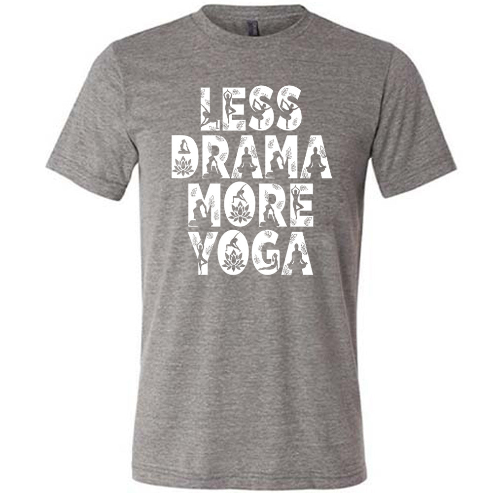 grey unisex tee with the words "less drama more yoga" on it, and within each letter there are silhouettes of people doing yoga poses as well as some lotus flowers and some leaves
