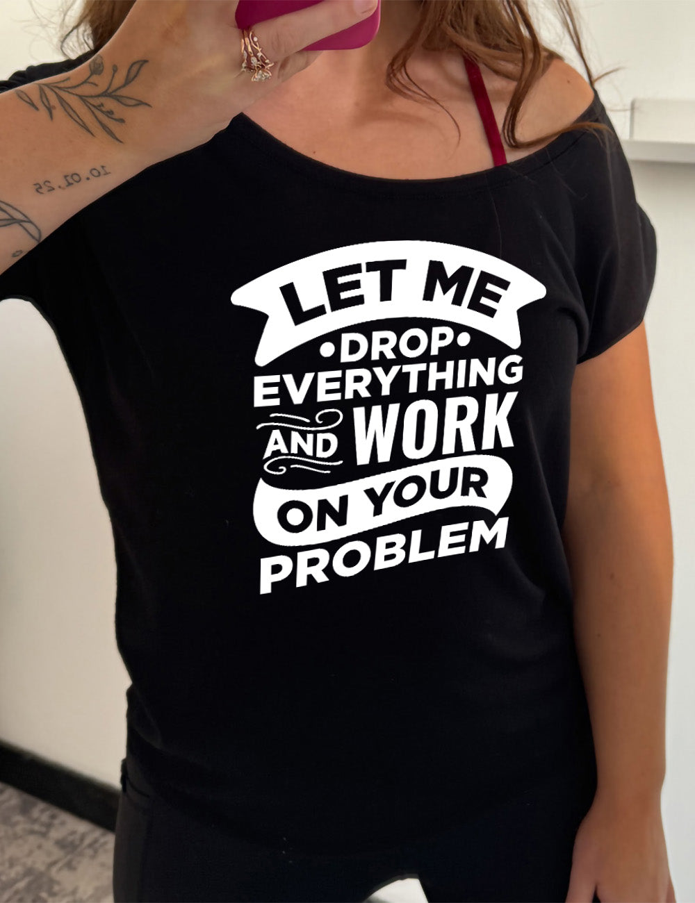 black slouchy tee with the words, some of them bannered or embellished, saying "Let me drop everything and work on your problem"