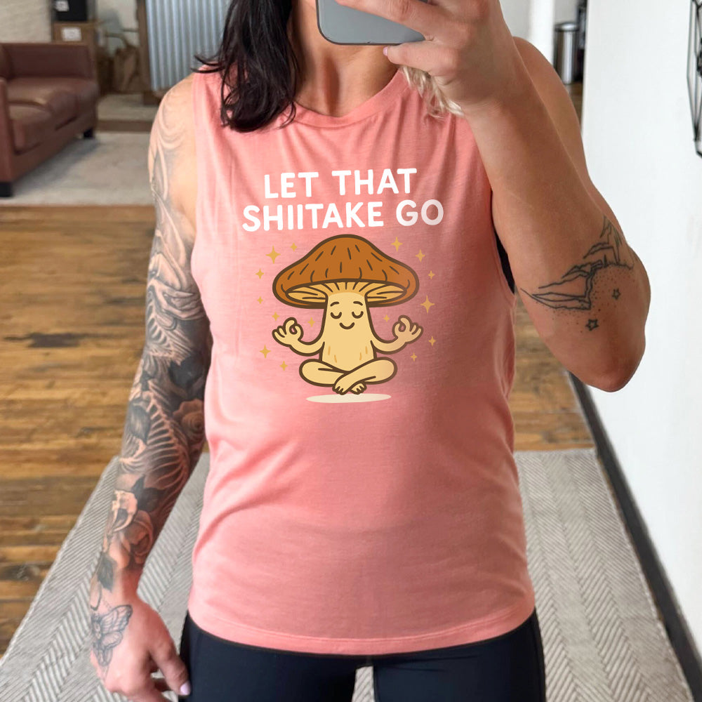 peach muscle tank with the words "let that shiitake go" on it and the graphic of a mushroom doing a yoga pose, surrounded by little stars