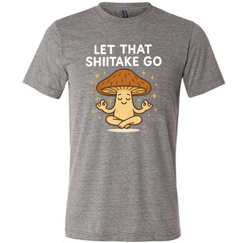 grey unisex tee with the words "let that shiitake go" on it and the graphic of a mushroom doing a yoga pose, surrounded by little stars