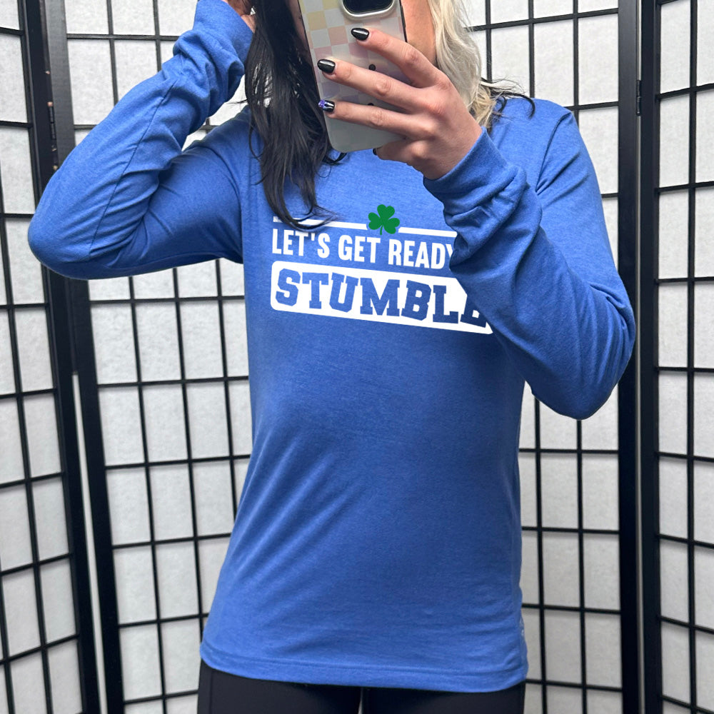 heather true royal long sleeve with the words "let's get ready to stumble" on it, with one little shamrock graphic, and the word "stumble" in a rectangular block, and the letters leaning in different directions