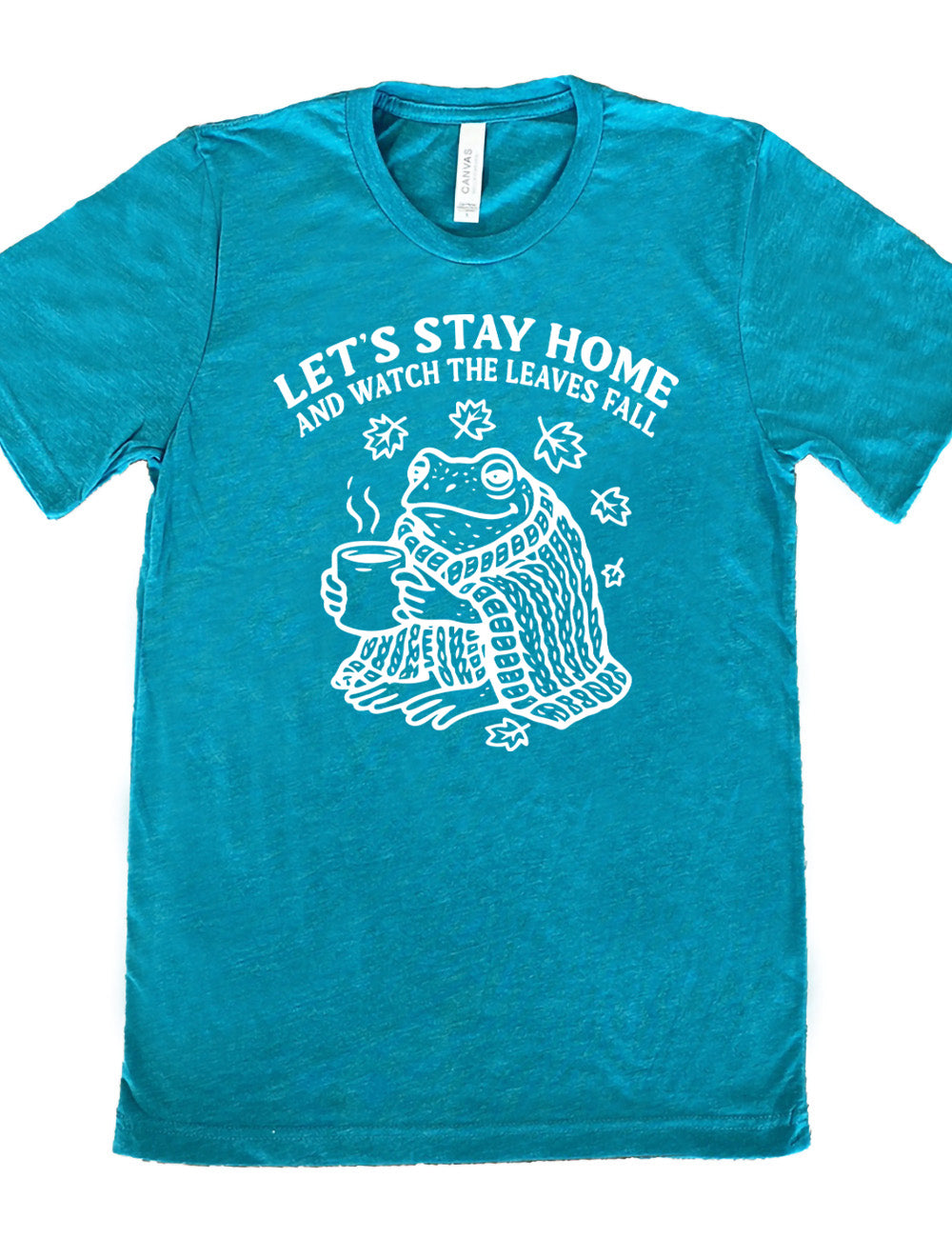 teal unisex tee with the words "let's stay home and watch the leaves fall" on it, and the graphic underneath of a frog, wrapped in a blanket, holding a mug of steaming beverage, with five leaves arching over it