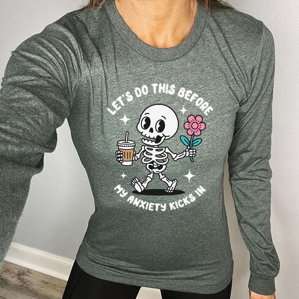 heather forest long sleeve shirt with the text "Lets Do This Before My Anxiety Kicks In" on it, and the graphic of a cartoon skeleton walking with a flower in one hand and a drink in the other
