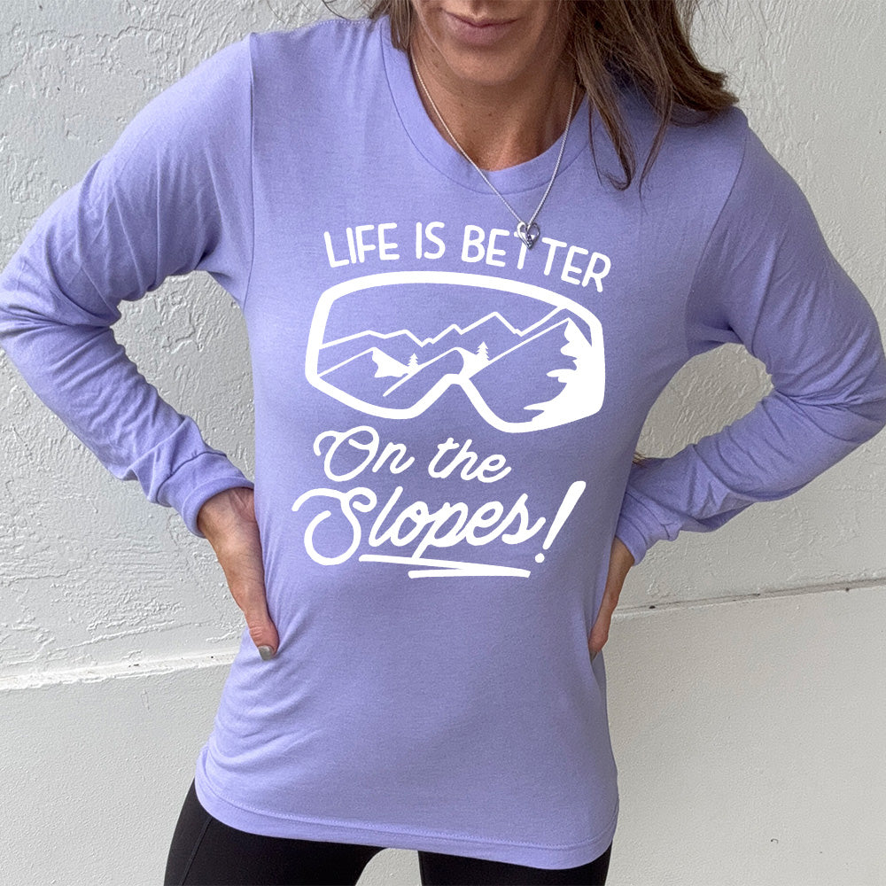 Heather dark lavender long sleeve with the words "Life is better on the slopes!" with the image of snow goggles and a reflection of the slopes in them