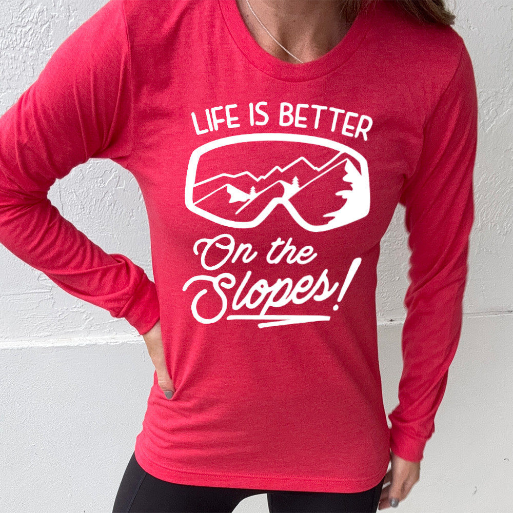 Heather red long sleeve with the words "Life is better on the slopes!" with the image of snow goggles and a reflection of the slopes in them