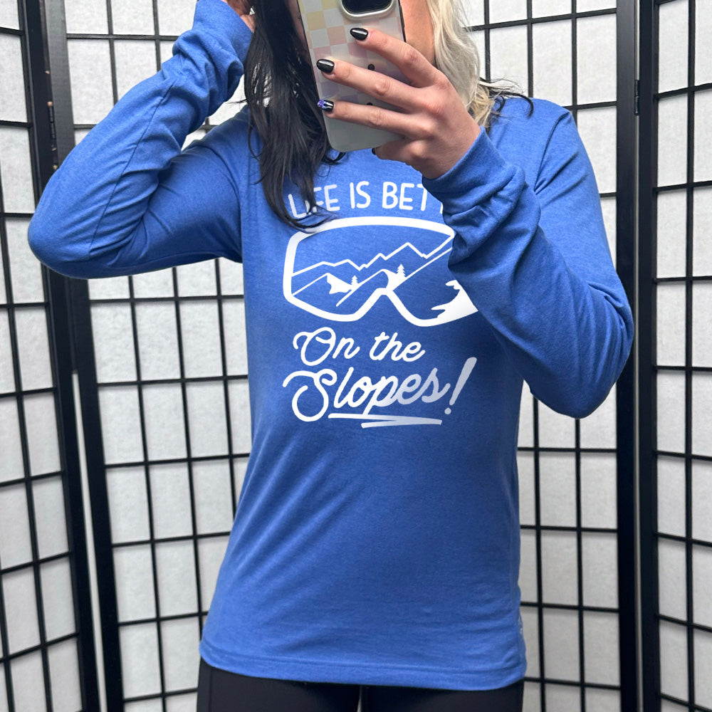 Heather royal blue long sleeve with the words "Life is better on the slopes!" with the image of snow goggles and a reflection of the slopes in them