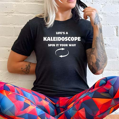 model wearing a black unisex shirt with the saying "Life's A Kaleidoscope Spin It Your Way" on it