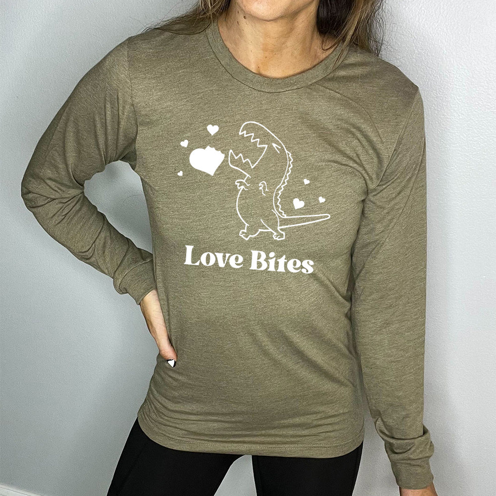 heather olive long sleeve shirt with the graphic of a dinosaur outline, eyes shut, mouth wide open, having bitten a chunk out of a heart, with a few other little hearts around it, and the text underneath saying "love bites"