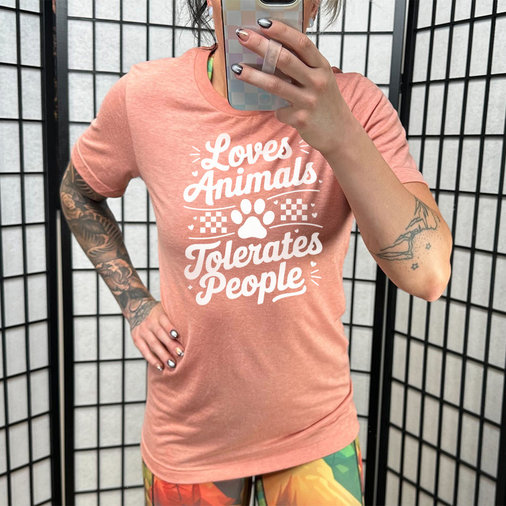 Model wearing sunset colored shirt with paw print and whickers graphic on it that says "Loves Animals Tolerates People"