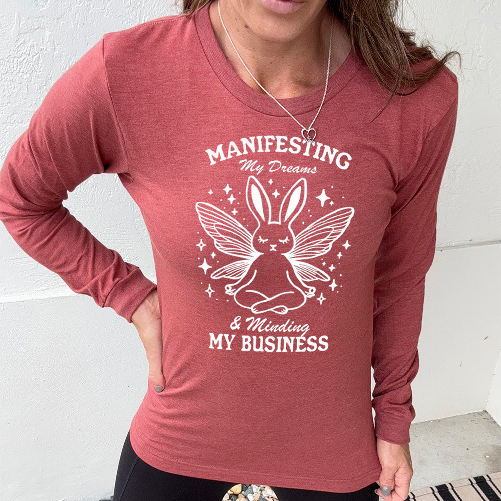 Heather clay long sleeve shirt with the words "Manifesting My Dreams & Minding My Business" and the graphic of a meditating rabbit with butterfly wings