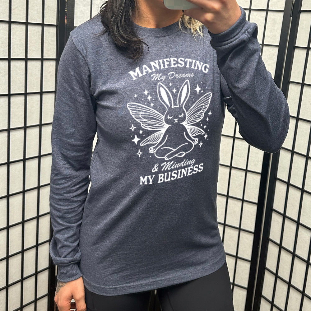 Heather navy long sleeve shirt with the words "Manifesting My Dreams & Minding My Business" and the graphic of a meditating rabbit with butterfly wings