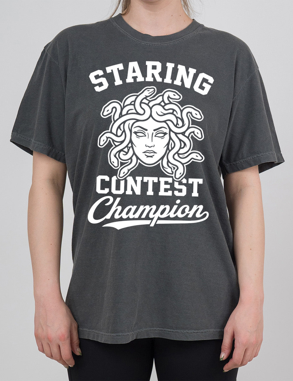 pepper modern tee with words surrounding the graphic of medusa's head saying "staring contest champion"
