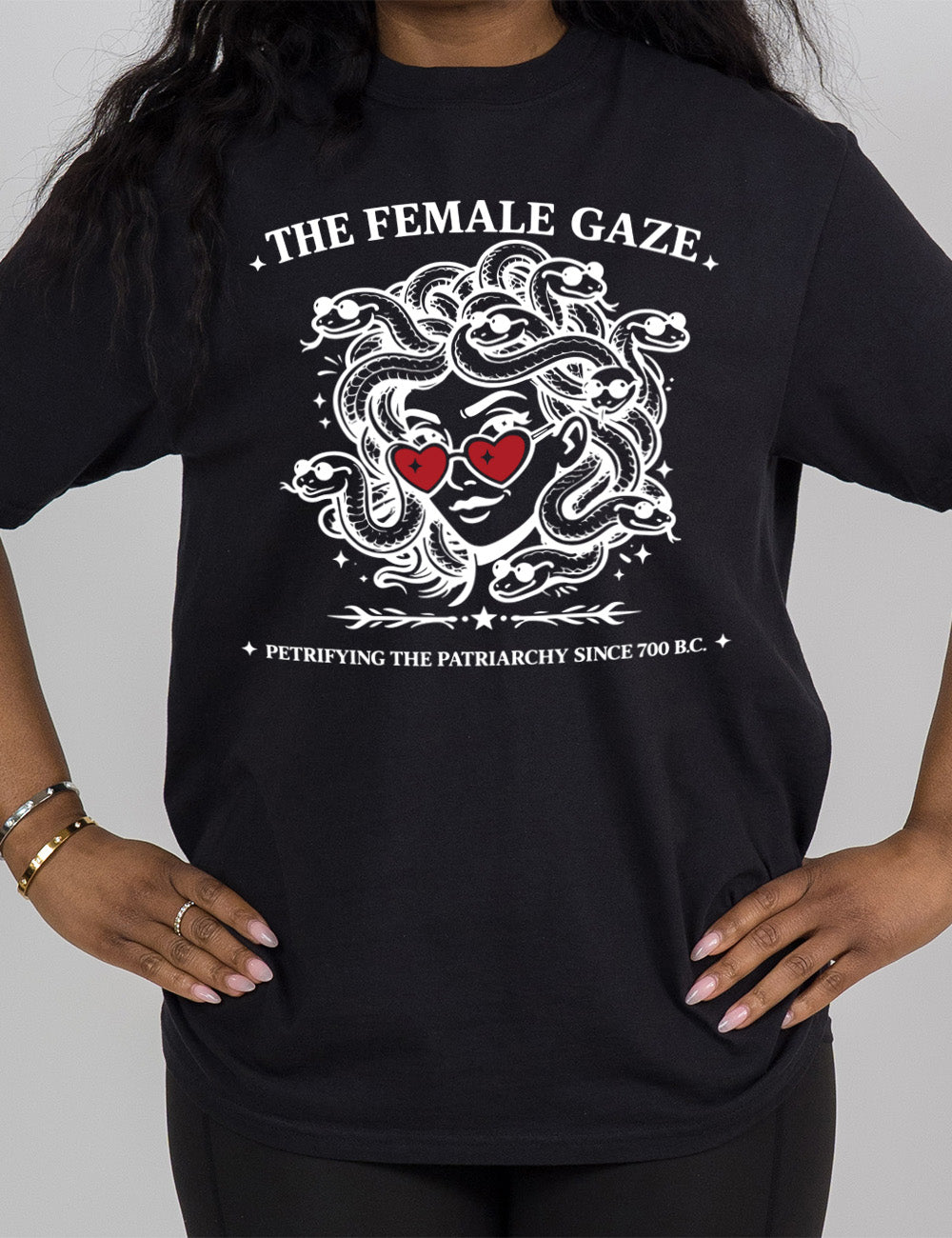 black modern tee with the detailed graphic of medusa, wearing red heart sunglasses, with sunglass-wearing snakes for hair, and the words above saying "THE FEMALE GAZE" with a little star on either end, and the smaller words below saying "petrifying the patriarchy since 700 B.C."