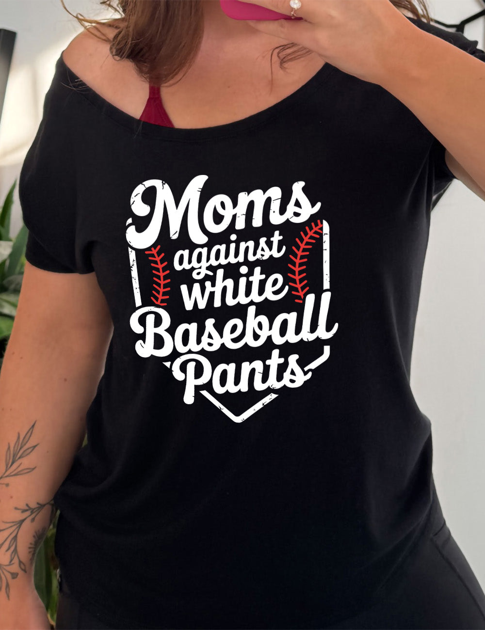 black slouchy tee with the words "moms against white baseball pants" on it, bordered by the baseball diamond, with baseball stitching on both sides of the words