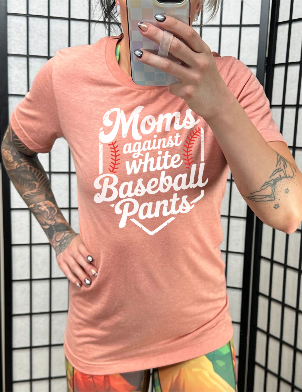 sunset unisex tee with the words "moms against white baseball pants" on it, bordered by the baseball diamond, with baseball stitching on both sides of the words