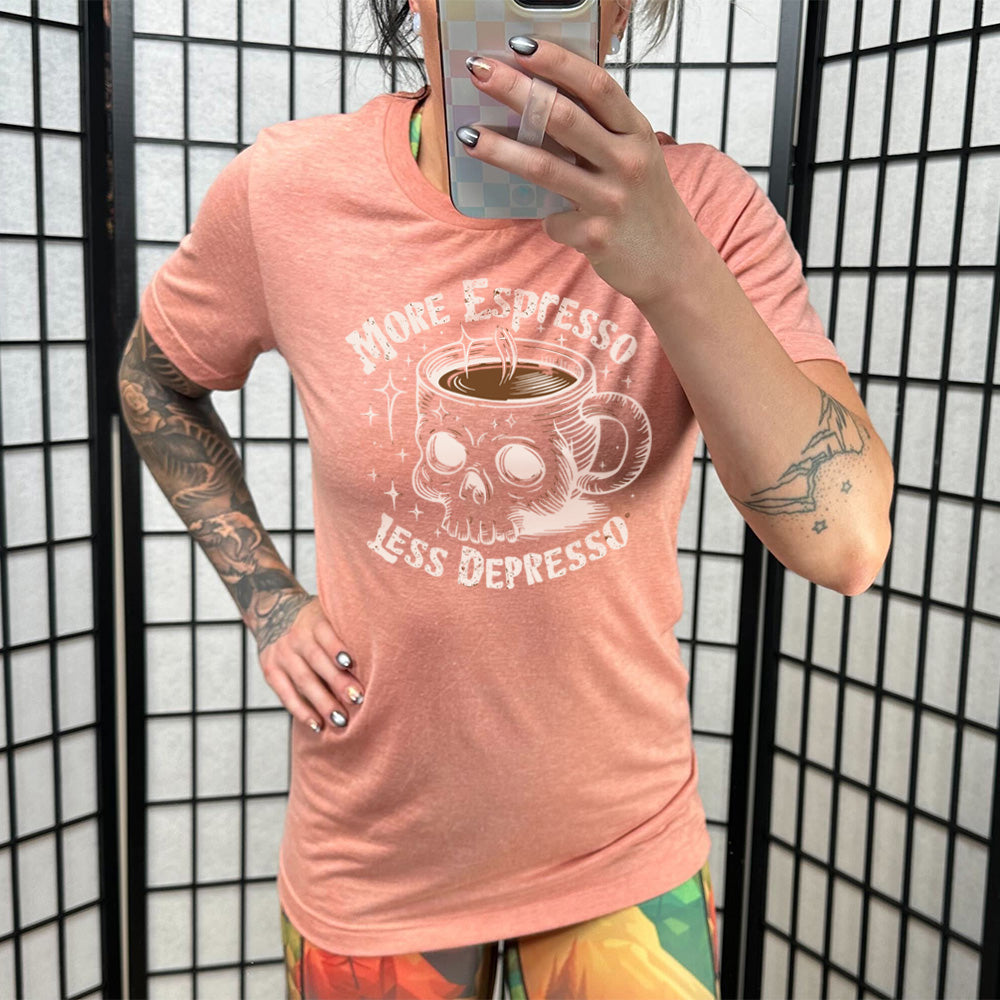 sunset unisex tee with the words "more espresso less depresso on it, around the graphic of a skull-shaped mug full of a steaming beverage, with lots of little stars around