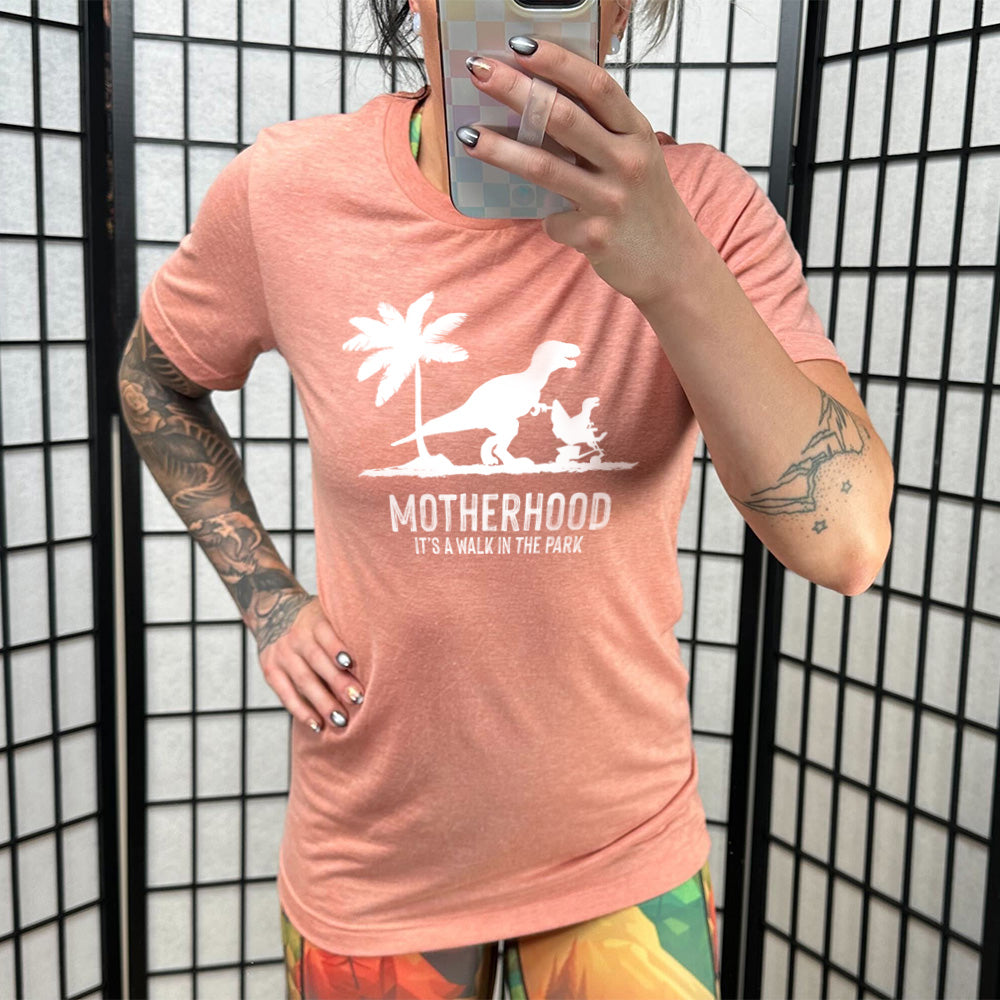 Sunset colored shirt with a mother and child dinosaur graphic on it that says "Motherhood, Its a Walk in the Park"