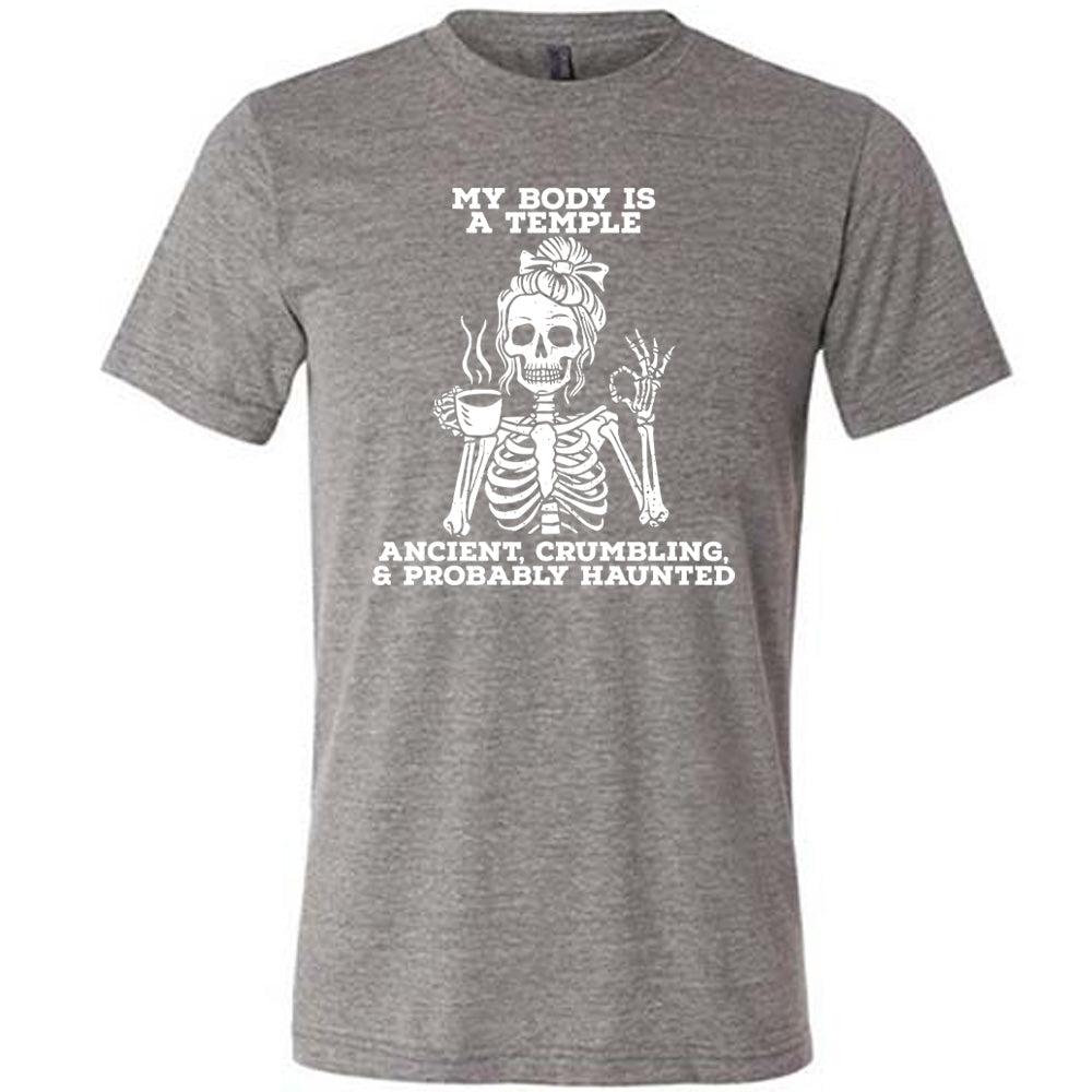 grey unisex tee with the words "My Body Is a Temple Ancient, Crumbling, & Probably Haunted" on it, with the graphic of a skeleton with its hair in a bow, with one hand holding steaming coffee, and the other giving the OK symbol