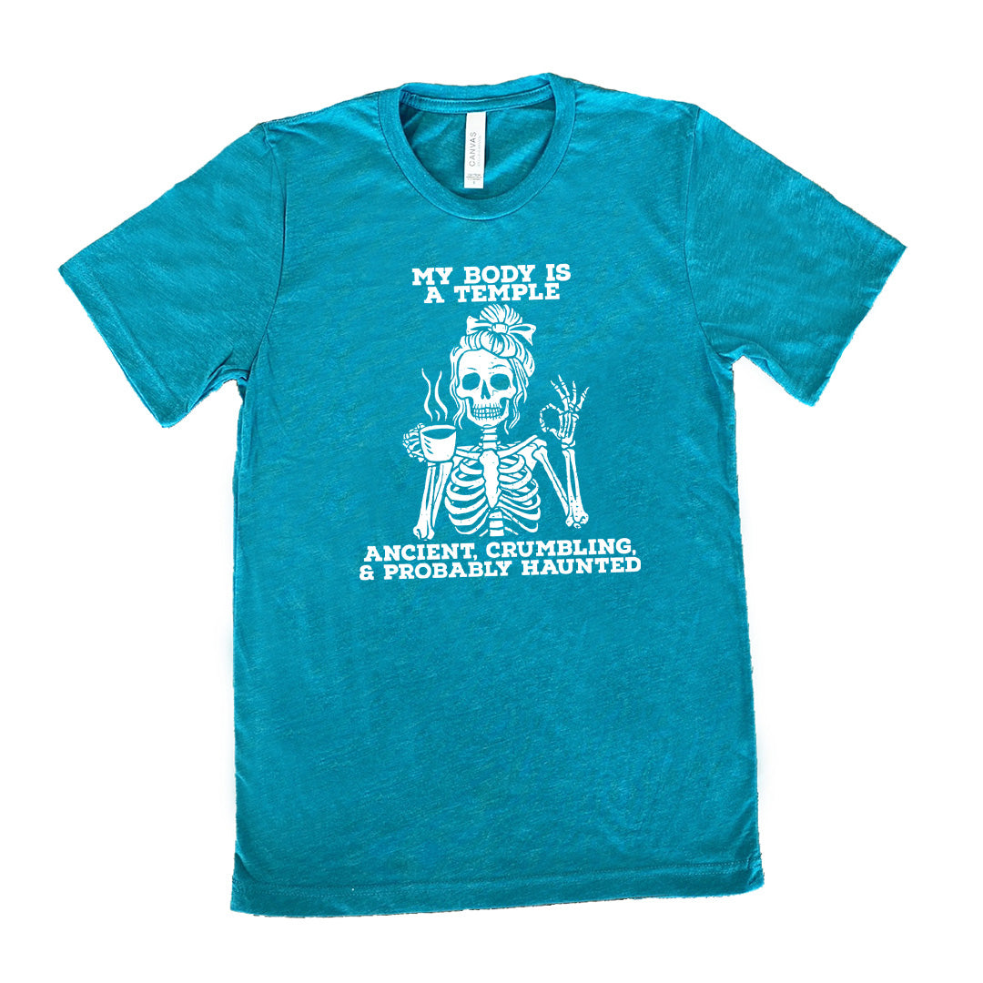 teal unisex tee with the words "My Body Is a Temple Ancient, Crumbling, & Probably Haunted" on it, with the graphic of a skeleton with its hair in a bow, with one hand holding steaming coffee, and the other giving the OK symbol