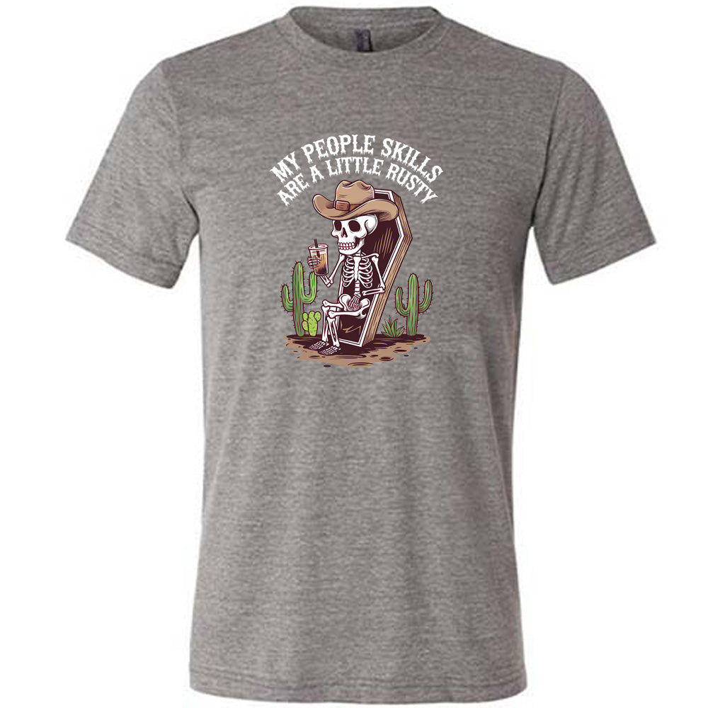 Grey colored shirt with a skeleton sitting in a coffin graphic on it that says "My People Skills Are A Little Rusty"