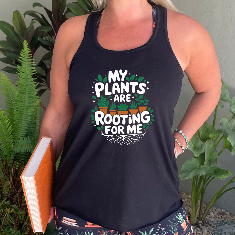Person wearing a black tank top with 'My plants are rooting for me' text, surrounded by plants.