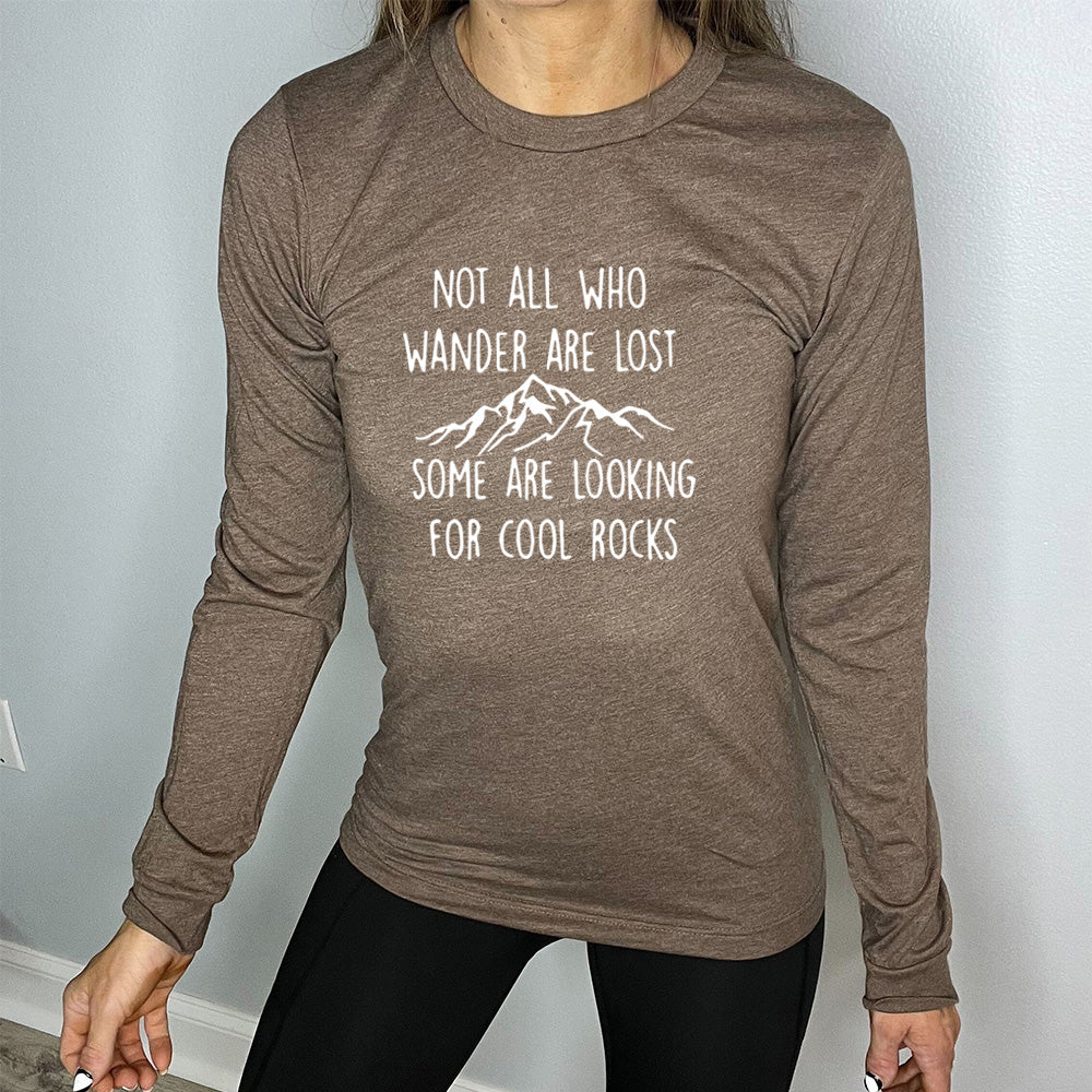 Brown colored long sleeve shirt with a mountain graphic on it that says "Not All Who Wander Are Lost Some Are Looking For Cool Rocks"