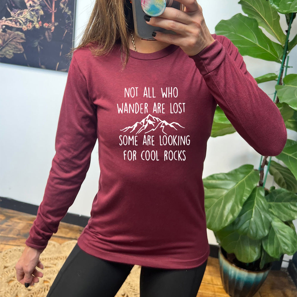 Heather cardinal long sleeve shirt with a mountain graphic on it that says "Not All Who Wander Are Lost Some Are Looking For Cool Rocks"