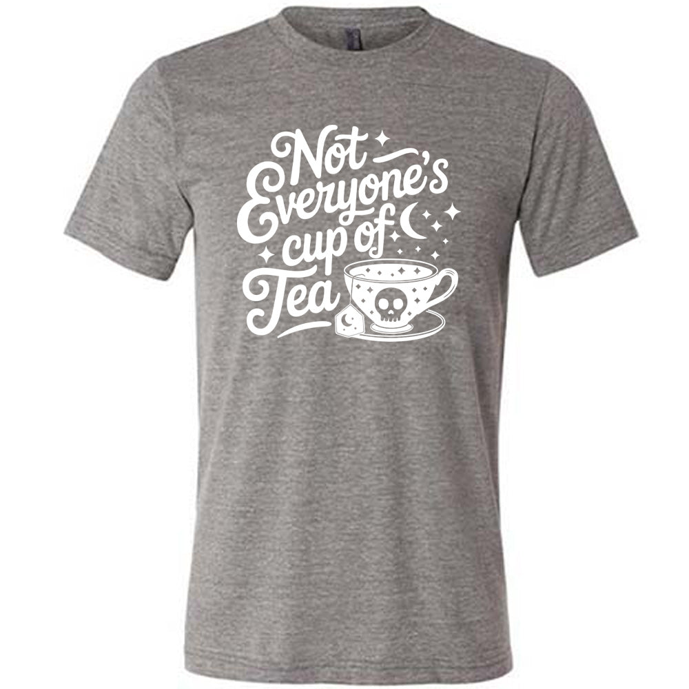 grey unisex tee with the words "not everyone's cup of a tea" in a cursive font, with the graphics of a moon and little stars, and a tea cup with a skull on it with stars and the tea bag has a moon on it