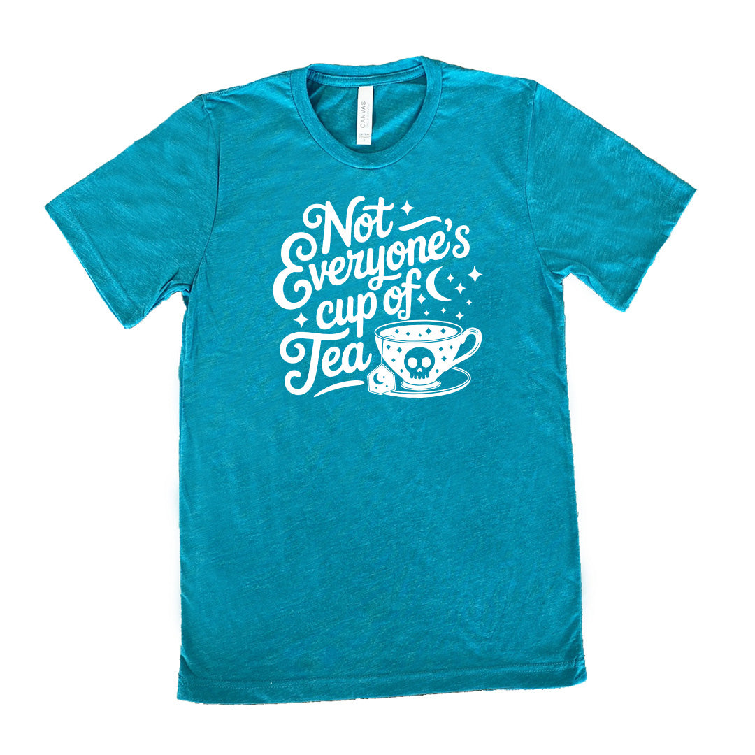 teal unisex tee with the words "not everyone's cup of a tea" in a cursive font, with the graphics of a moon and little stars, and a tea cup with a skull on it with stars and the tea bag has a moon on it