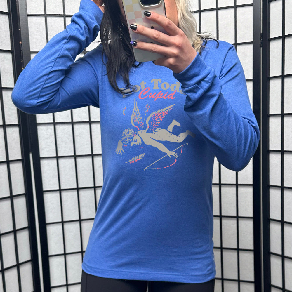 heather true royal long sleeve shirt with the words "not today, Cupid" on it, with the graphic of cupid, presumably dead, lying on the ground, bow at his side, with an arrow through his back