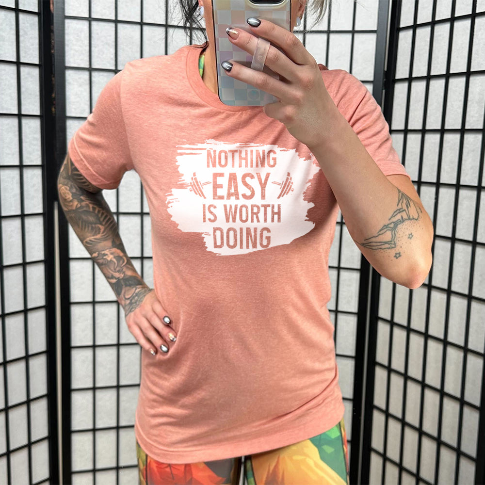 Sunset Unisex Tee, with wording Nothing Easy is Worth Doing, lettering is color of shirt with barbells all over a white patch