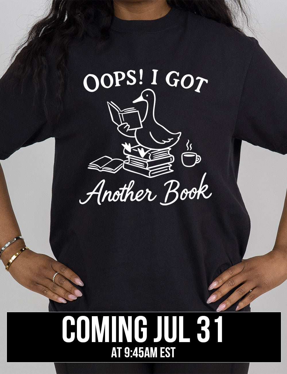 black modern tee with the graphic of a goose, sitting on a stack of books, reading a book, with another book open beside the stack, and a steaming cup of coffee on the other side, with the words around the graphic saying "Oops! I got another book" , coming july 31st