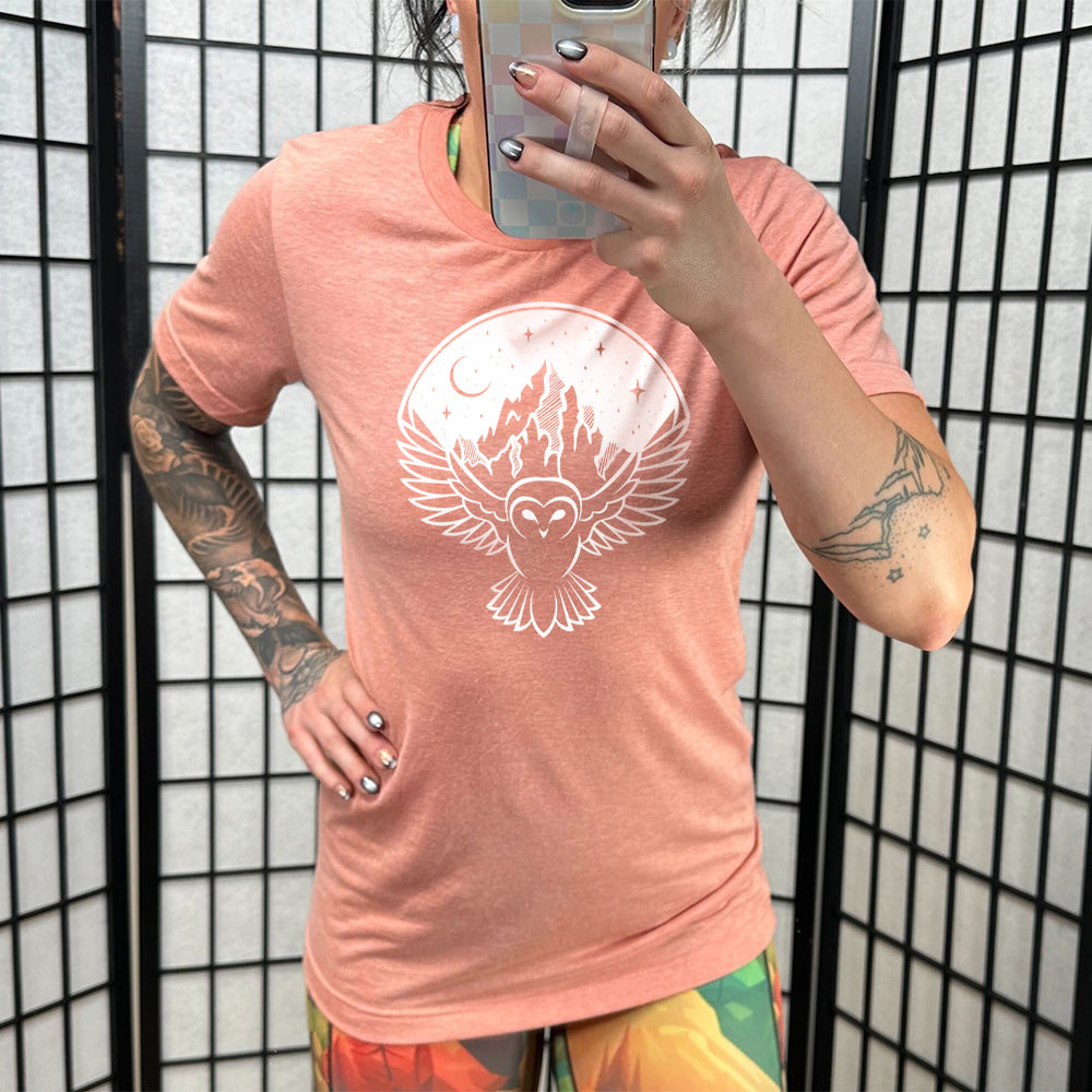 Model wearing sunset colored shirt with night sky owl and mountain graphic on it