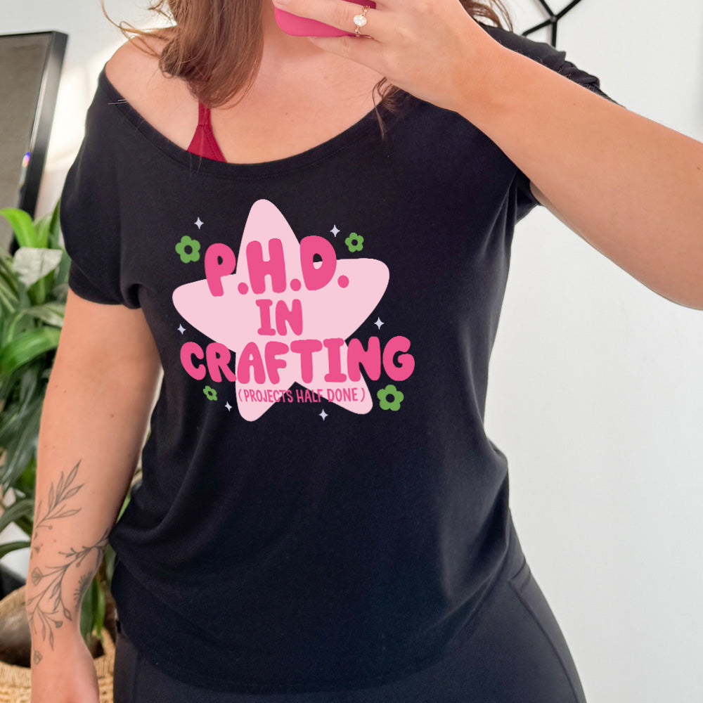 black slouchy tee with cartoon graphic of a large star behind the words "P.H.D. in Crafting" in large font with the words (Projects Half Done) in small font underneath, with very small flowers and stars around