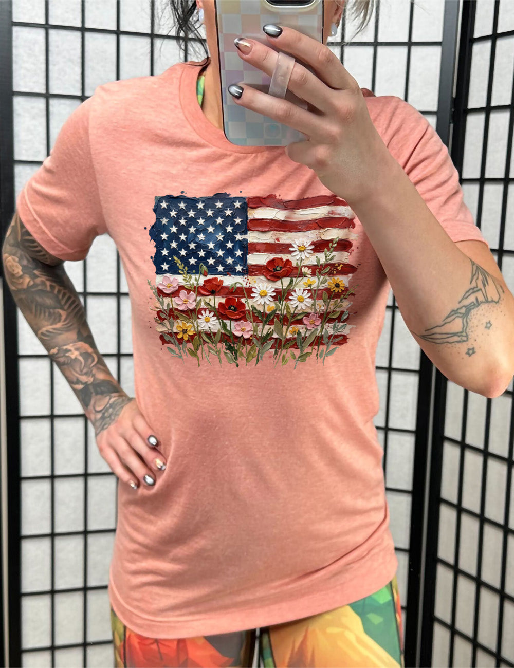 sunset unisex tee with the graphic of an American flag with flowers in front of it, with the style of the graphic looking made of oil paint