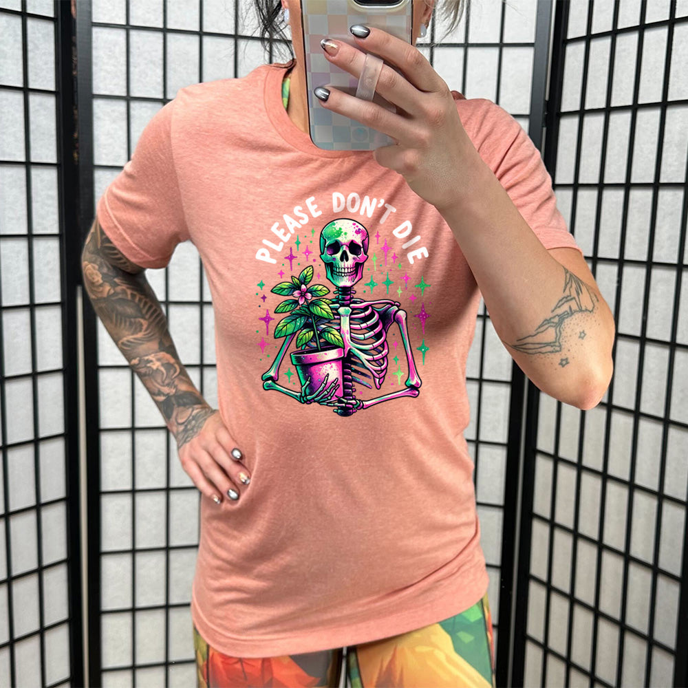 Model wearing sunset colored shirt with a skeleton holding a plant graphic on it that says "Please Don't Die"