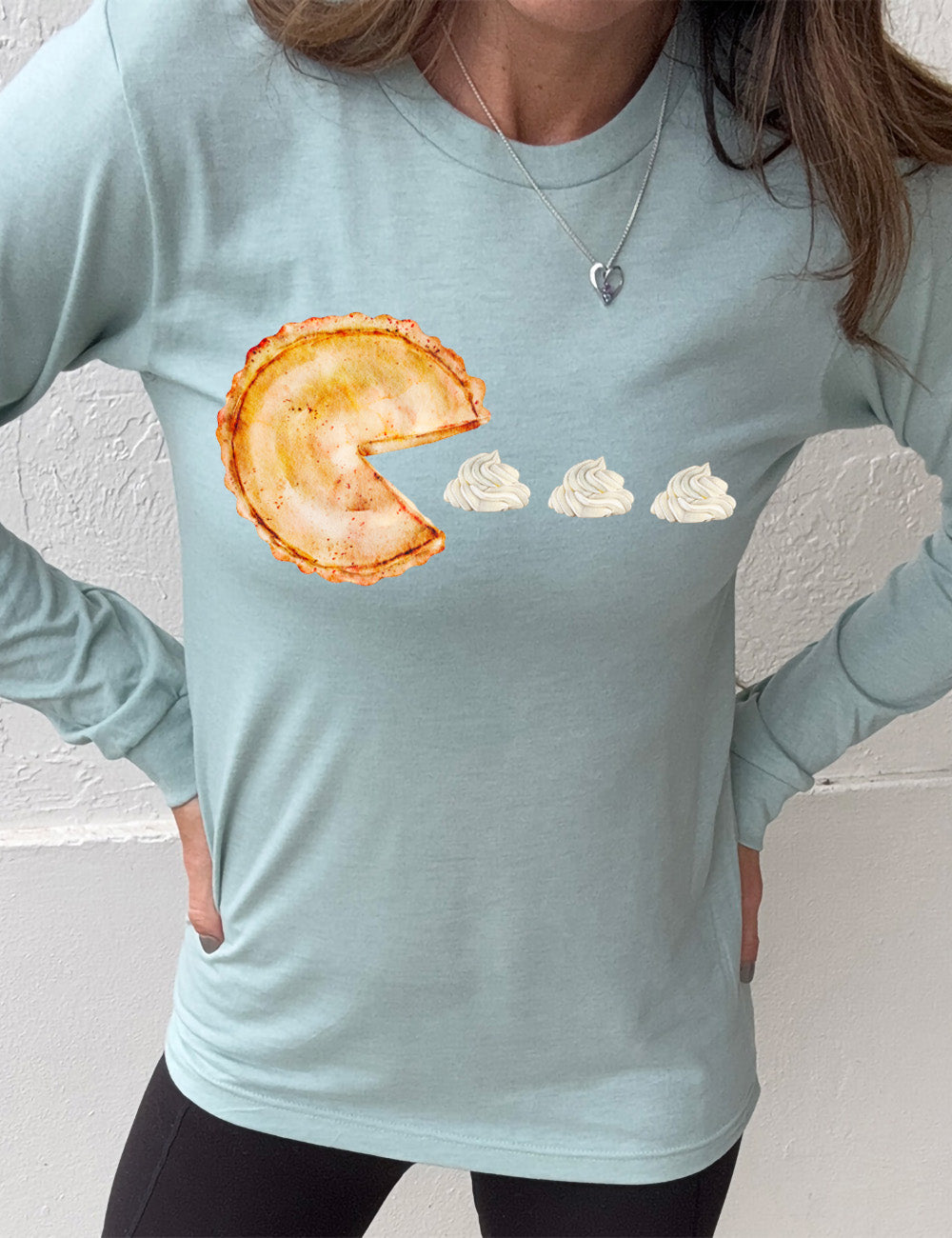 heather dusty blue long sleeve tee with the graphic of a pumpkin pie, with the a slice taken out of it so that it looks like Pacman, heading in the direction of three dollops of whipped cream