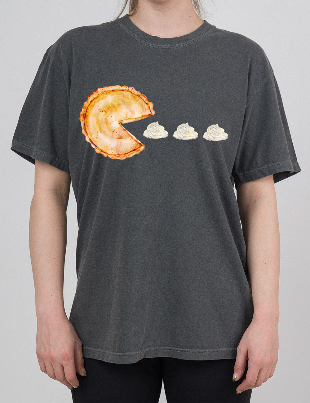 pepper modern tee with the graphic of a pumpkin pie, with the a slice taken out of it so that it looks like Pacman, heading in the direction of three dollops of whipped cream
