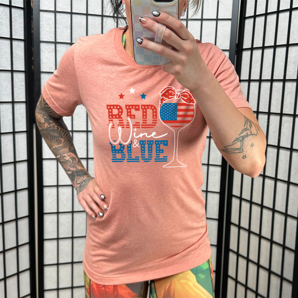 Model wearing sunset colored shirt with an American flag wine glass graphic on it that says "Red Wine & Blue"