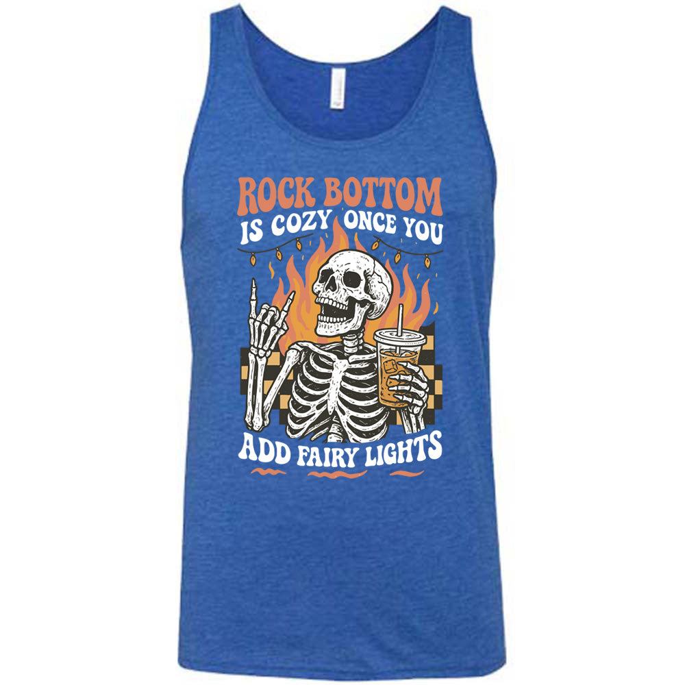 blue unisex tank with the words "rock bottom is cozy once you add fairy lights" with the graphic of a skeleton giving the rocker sign with one hand while holding an iced drink in the other, with a background of some checkerboard, some flames, and a string of fairy lights above the flames