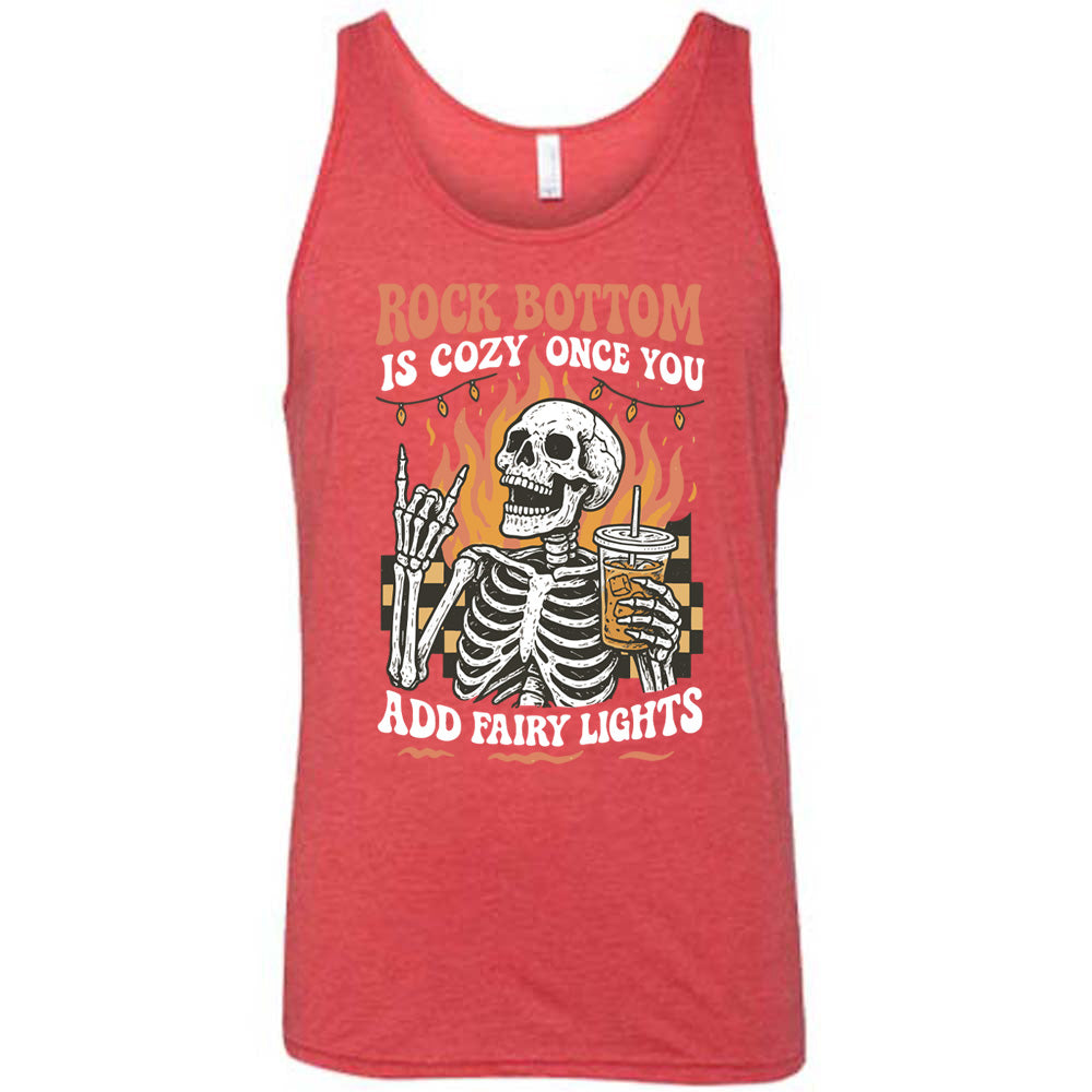 red unisex tank with the words "rock bottom is cozy once you add fairy lights" with the graphic of a skeleton giving the rocker sign with one hand while holding an iced drink in the other, with a background of some checkerboard, some flames, and a string of fairy lights above the flames