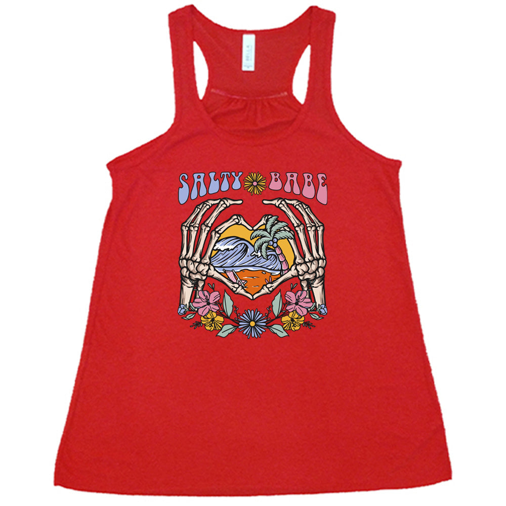 Red colored flowy tank with a skeleton heart hands around ocean waves graphic on it that says "Salty Babe"