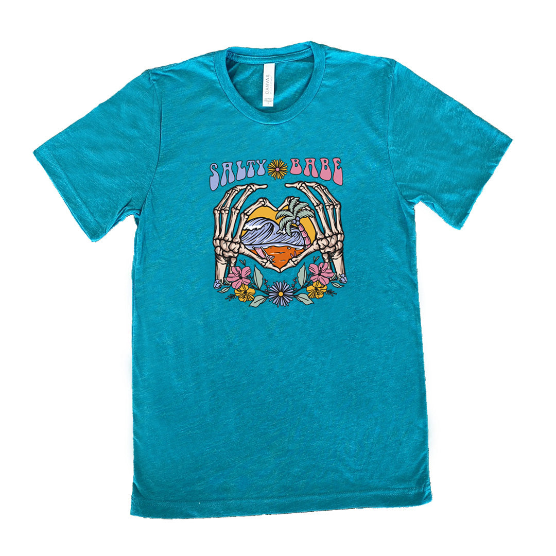 Teal colored shirt with a skeleton heart hands around ocean waves graphic on it that says "Salty Babe"