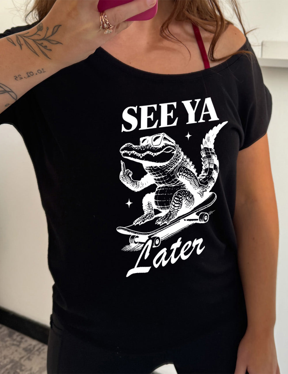 black slouchy tee with the graphic of an alligator, riding a skateboard, wearing sunglasses, and giving the middle finger, surrounded by the words saying "see ya later"