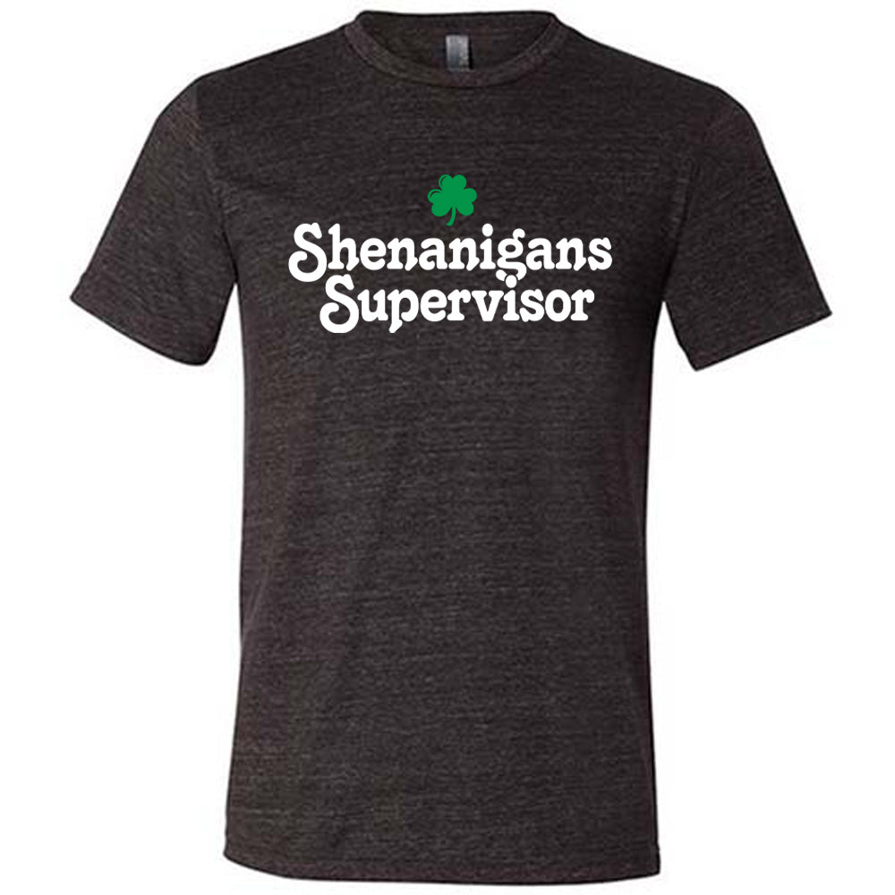 black unisex tee with the words "shenanigans supervisor" on it, with one small clover graphic above it