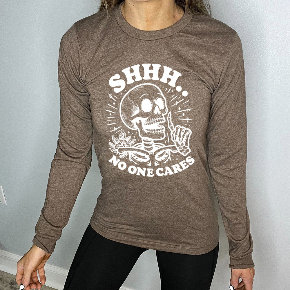 heather brown long sleeve with the words "Shhh.. no one cares" on it, with the graphic of a skeleton holding a finger to its lips