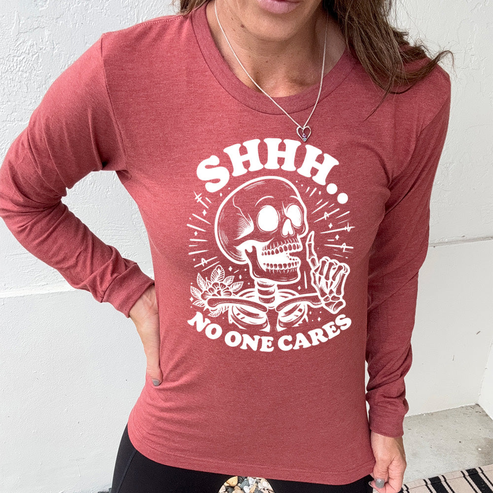 heather clay long sleeve with the words "Shhh.. no one cares" on it, with the graphic of a skeleton holding a finger to its lips